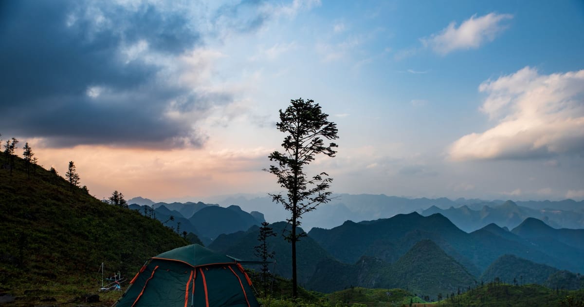 A small tent pitched on a hillside in evening light.