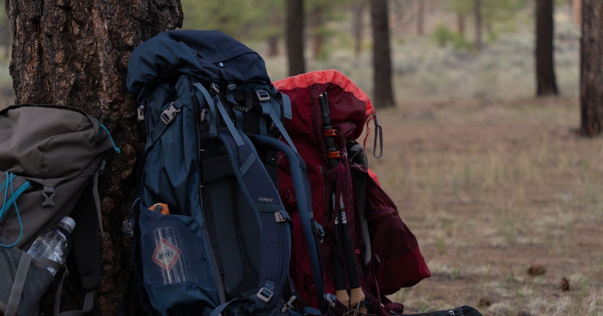 A backpack, tent, sleeping bag and mat laid out on the ground.